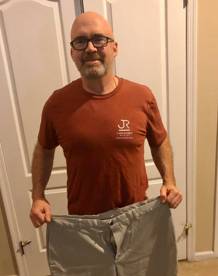 Chris holds up an old pair of pants to show off his transformation made possible through fitness and nutrition.